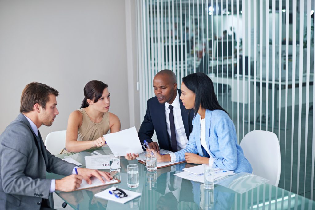 Four business professionals sit at a glass table in an office, discussing email lists for effective marketing and making strategic decisions as directors of marketing
